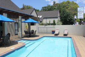 una piscina con sillas, mesas y sombrillas en Bethlehem Motor Inn and Conference Centre, en Tauranga