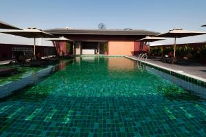 a swimming pool with green water and umbrellas at Casa Nithra Bangkok in Bangkok