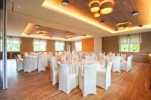 Un salón de banquetes con mesas y sillas blancas. en Landhotel Kuralpe Kreuzhof, en Lautertal