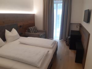 ein Schlafzimmer mit einem weißen Bett, einem Stuhl und einem Fenster in der Unterkunft Hotel Krone in Bruneck