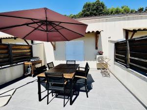 un patio con mesa de madera, sillas y sombrilla en Propriété Malva appartement agava, en Alata