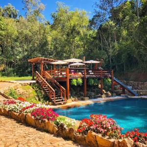 a pool with a pavilion and flowers in front of it at Hotel Pousada Riacho da Areia in Águas de Lindoia