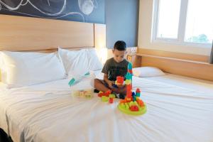 um rapaz sentado numa cama com os seus brinquedos em Ibis Porto Alegre Assis Brasil em Porto Alegre