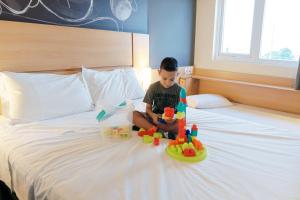 un joven sentado en una cama con sus juguetes en Ibis Porto Alegre Assis Brasil, en Porto Alegre