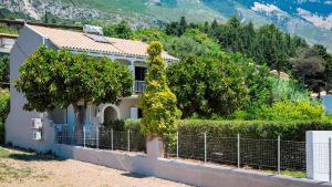 a house with a fence and trees and mountains at Beachfront Suites Lourdas in Lourdata