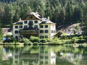 a large house sitting next to a body of water at Hotel Baur Am See in Dobbiaco