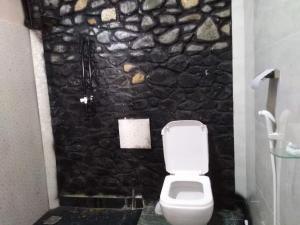 a bathroom with a white toilet and a stone wall at ARROW Haputale village inn in Haputale