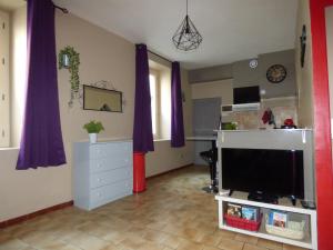 a living room with a tv and purple curtains at Chez Odile in Sigean