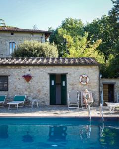 a woman sitting in front of a house with a pool at Querceto Di Castellina in Castellina in Chianti