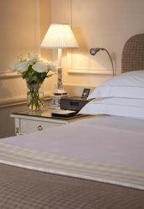 a bed with a table with a lamp and a vase of flowers at The Merrion Hotel in Dublin