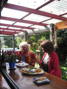 Duas mulheres sentadas à mesa a comer comida. em Moanarua Beach Cottage em Ohope Beach