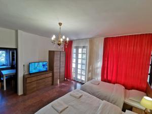 ジュラにあるAmbient Deluxe Apartmanの赤いカーテン、ベッド、テレビが備わるベッドルーム1室が備わります。