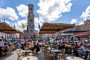 um grupo de pessoas sentadas em mesas em uma cidade com uma torre do relógio em Hotel Central em Bruges