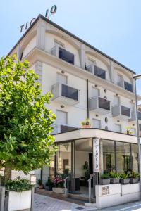 ein hohes weißes Gebäude mit einem Baum davor in der Unterkunft Hotel Tiglio in Rimini