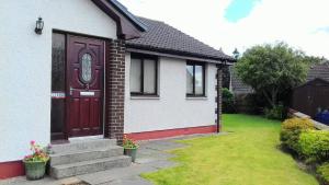 una casa blanca con una puerta roja y un patio en Clisham, en Beauly