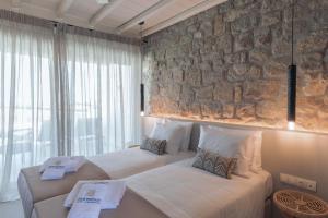 Aegean Hospitality في مدينة ميكونوس: سريرين في غرفة بجدار حجري