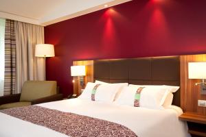 um quarto de hotel com uma cama e uma parede vermelha em Holiday Inn Lille Ouest Englos, an IHG Hotel em Englos