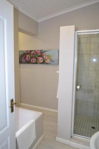 La salle de bains est pourvue d'une douche et d'une baignoire blanche. dans l'établissement By The Way Guesthouse, à Clarens