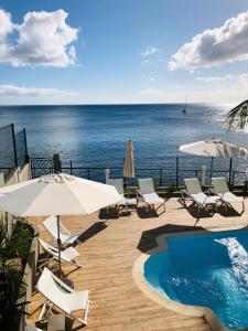 a swimming pool with chairs and umbrellas and the ocean at Hotel Pelican in Schœlcher