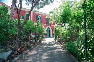 un percorso che conduce a un edificio rosso con alberi e piante di Villa Ulisse a Ercolano