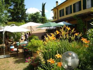 einen Garten mit Tischen, Stühlen, Sonnenschirmen und Blumen in der Unterkunft Tenuta Poggio alla Farnia in Fauglia