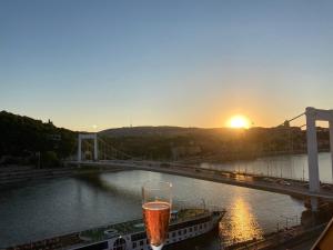 una bebida sentada en un balcón con la puesta de sol en el fondo en Riverside flat with King Castle view, en Budapest