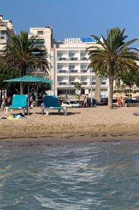 a beach with two blue chairs and a hotel at Hotel Vela in Roses