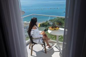 a woman sitting in a chair on a balcony looking at the ocean at Poseidon The Beach Hotel in Budva