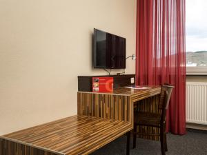 een kamer met een bureau, een televisie en een rood gordijn bij hotelo Heidelberg in Heidelberg