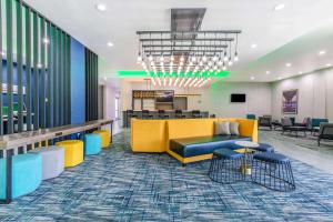a lobby with a yellow couch and tables and chairs at La Quinta Inn & Suites by Wyndham Galveston West Seawall in Galveston