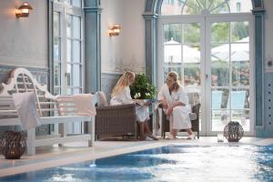 twee vrouwen die rond een tafel naast een zwembad zitten bij 4-Sterne Superior Erlebnishotel Bell Rock, Europa-Park Freizeitpark & Erlebnis-Resort in Rust