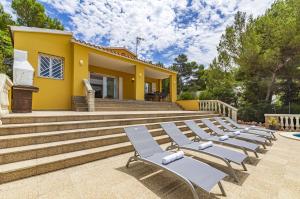 a row of lounge chairs in front of a yellow house at Villa Novas Park in Son Parc