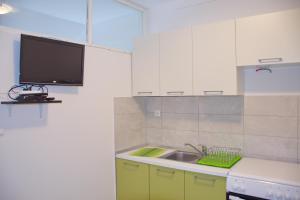 a kitchen with white cabinets and a sink and a tv at Apartmani Vidušin in Novalja