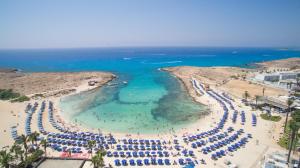 an aerial view of a beach with blue umbrellas and the ocean at Anonymous Beach Hotel (Adults 16+) in Ayia Napa