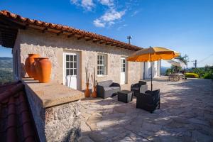 um pátio com um guarda-sol e cadeiras e uma casa em Casa d' Avó Marcelina - Casas de Campo em Arcos de Valdevez