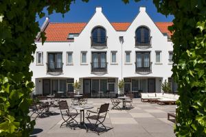 un grand bâtiment blanc avec une cour dotée de tables et de chaises dans l'établissement Strandhotel Wilhelmina, à Domburg