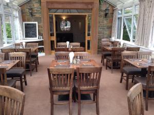 een restaurant met houten tafels, stoelen en ramen bij Arden House Hotel in Kirkcudbright