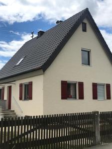 Casa blanca con ventanas rojas y valla en Ferienhaus -HAUS DER WEICHSEL- bei Lauingen, mit Sauna en Veitriedhausen