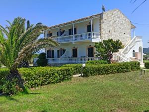 a large white house with a palm tree in front of it at Elli Beach Apartments and Studios in Almiros Beach