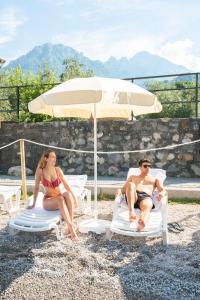 Ein Mann und eine Frau, die auf Gartenstühlen unter einem Schirm sitzen in der Unterkunft Park Hotel Abbadia in Abbadia Lariana