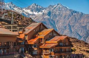 a building with snow capped mountains in the background at GMVN Auli in Joshīmath