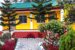 a yellow and red house with trees and flowers at Jaldapara Inn Resort in Mādāri Hāt