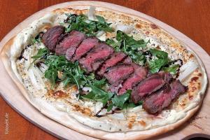 a pizza with meat and greens on a table at Ferienwohnung Biewer in Trier