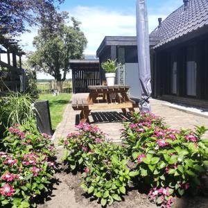 un patio con un banco de madera y flores rosas en ons huusie, en Noord-Sleen