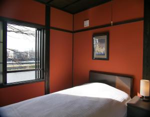 a bedroom with orange walls and a bed and a window at Saigawa House in Kanazawa