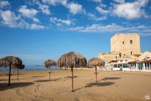 un gruppo di ombrelloni di paglia su una spiaggia con un edificio di a Pozzallo vicino al mare a Pozzallo