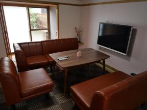 a living room with leather furniture and a flat screen tv at SAKURA Aburaya in Takayama