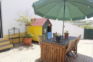 a wooden table with a green umbrella and a dog house at Casinha da Andorinha - Ericeira in Ericeira