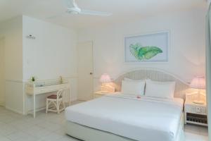 a white bedroom with a bed and a desk at Equator Village Resort in Gan