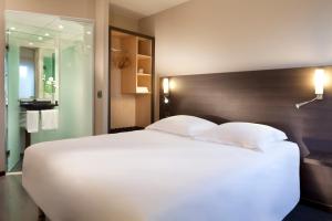 sypialnia z dużym białym łóżkiem z drewnianym zagłówkiem w obiekcie Escale Oceania Nantes Aéroport w mieście Bouguenais